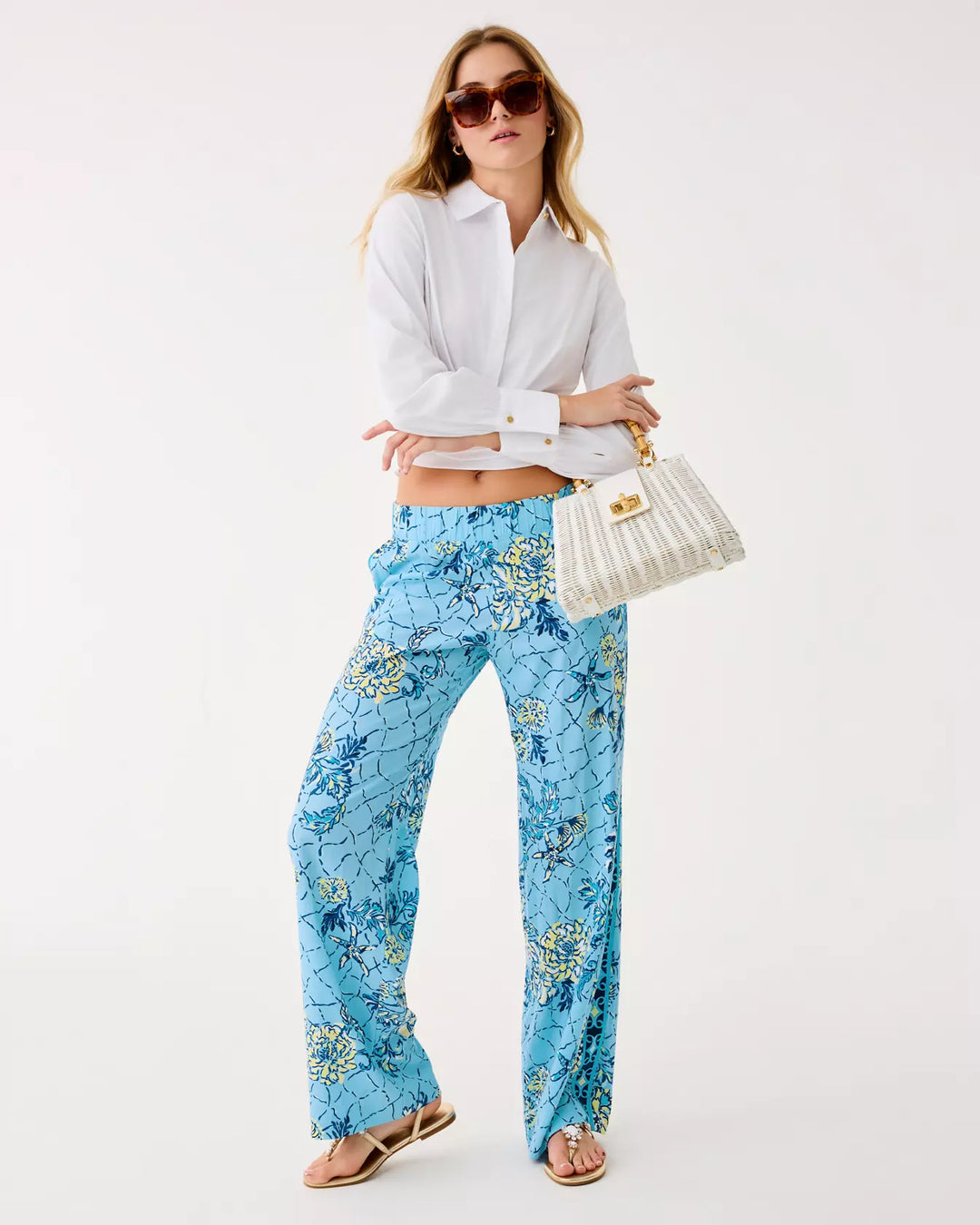 Woman wearing a white shirt and blue floral pants with a white handbag on a white background