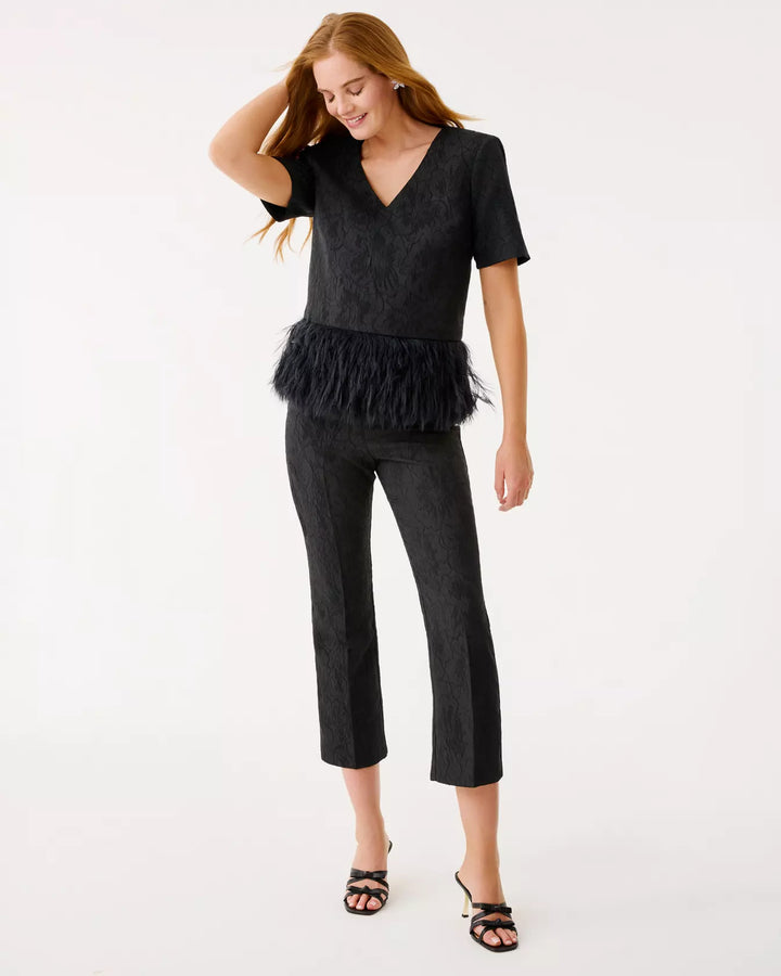 Woman wearing a black top with ruffled details and black pants on a white background