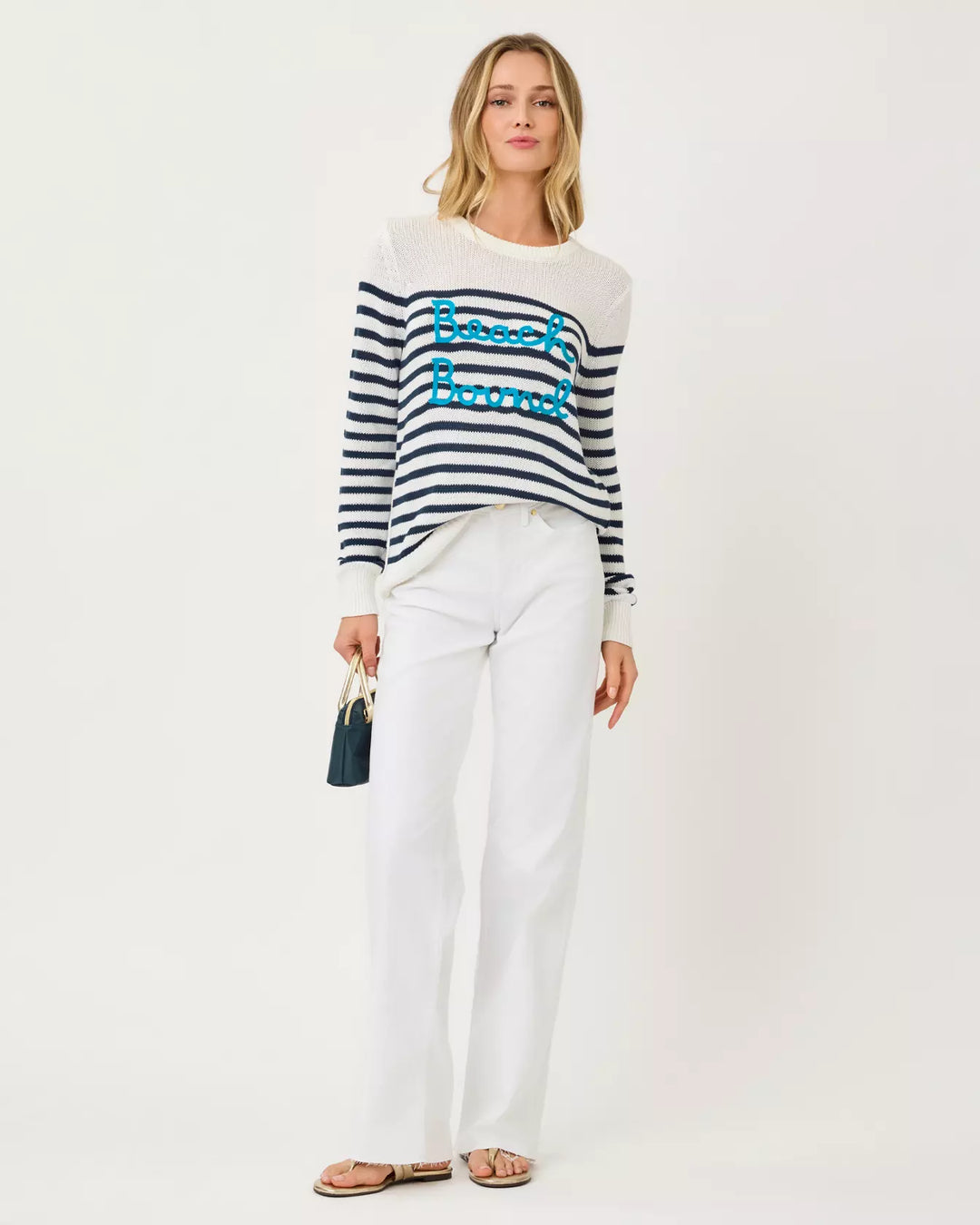 Woman wearing a striped sweater with text and white pants on a white background