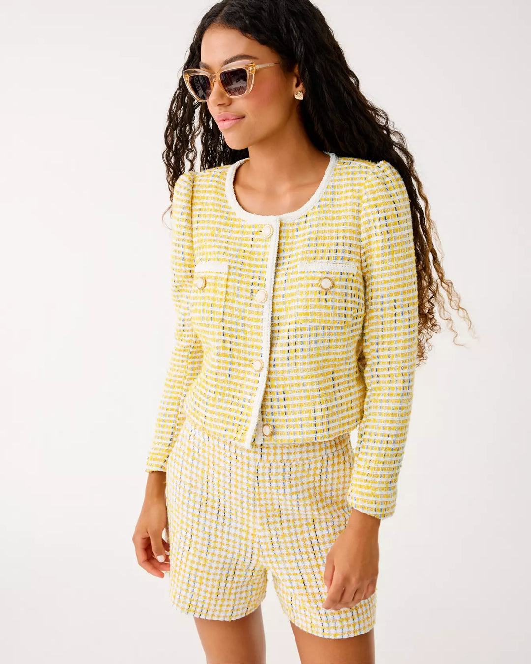 Woman wearing a yellow checkered suit with sunglasses on a white background