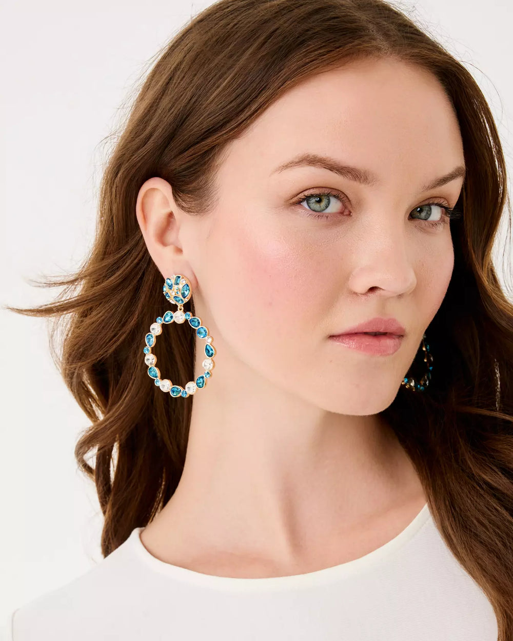 Woman wearing large hoop earrings with  blue gemstones on a white background