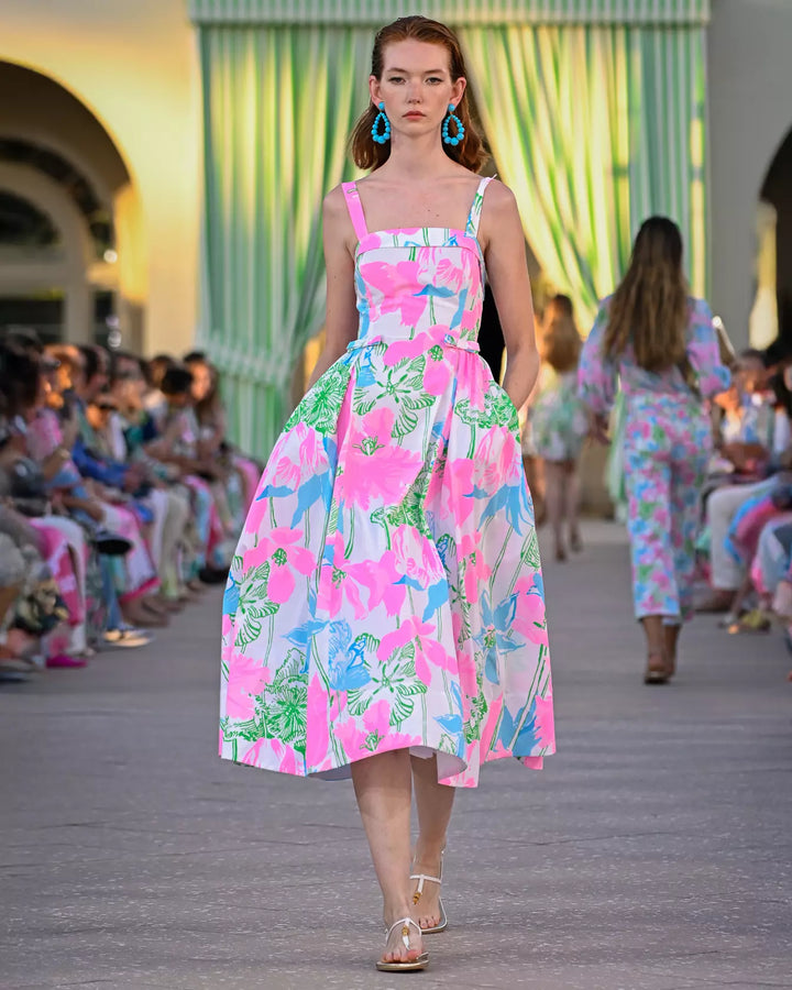 Model walking on a runway wearing a colorful floral dress.